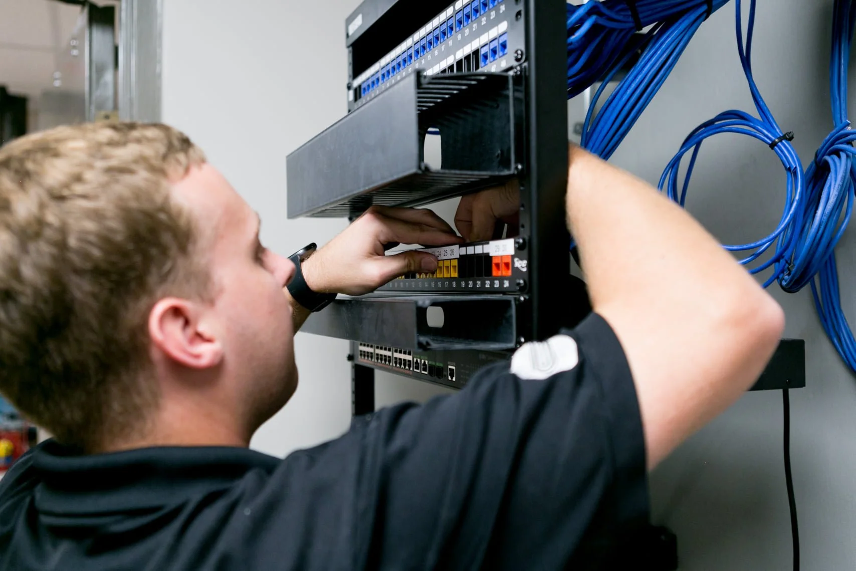 A technician installing or maintaining wiring in a network rack, with blue Ethernet cables connected to network equipment.