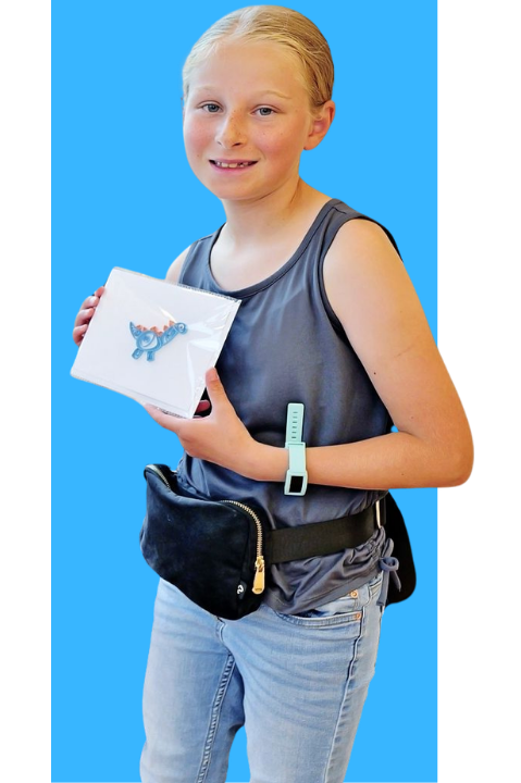 A young girl with blonde hair in a ponytail, wearing a sleeveless gray top, holding a small package with a blue dinosaur sticker, and wearing a waist pouch and watch, standing against a blue background.