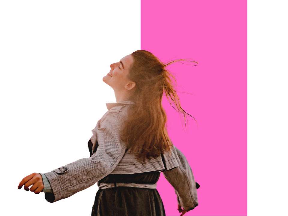 A woman with red hair smiling with her eyes closed and head tilted back, standing against a background split vertically between black and pink.