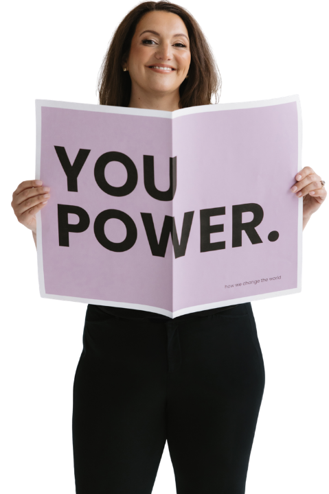 Woman with shoulder-length brown hair smiling and holding a large purple sign that says "You Power."