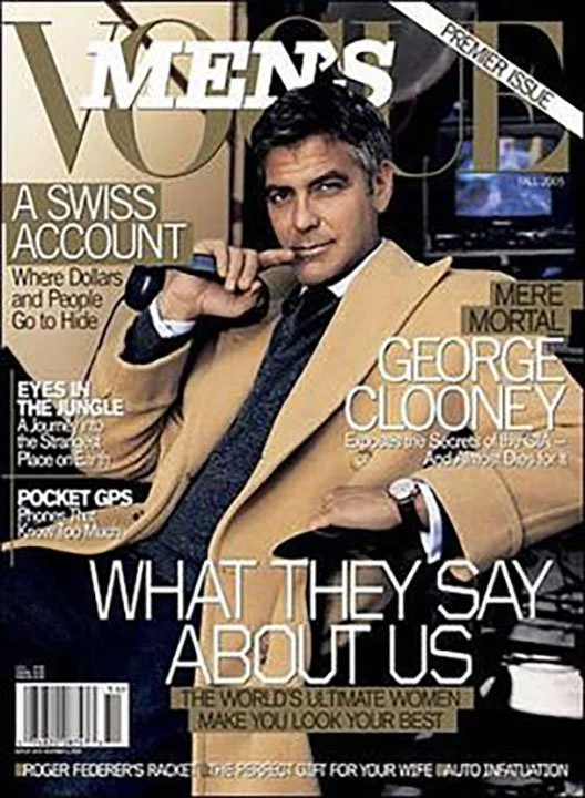 Cover of Men's Vogue magazine featuring actor George Clooney in a beige coat and dark suit, holding a cigar, with various headlines about men and lifestyle.