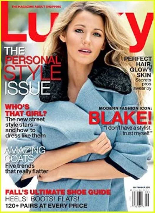 Close-up of a woman with blonde hair, wearing a light blue coat with black collar details, on the cover of a fashion magazine titled 'LUXY'. The magazine features headlines about fashion, style, and beauty across the cover.
