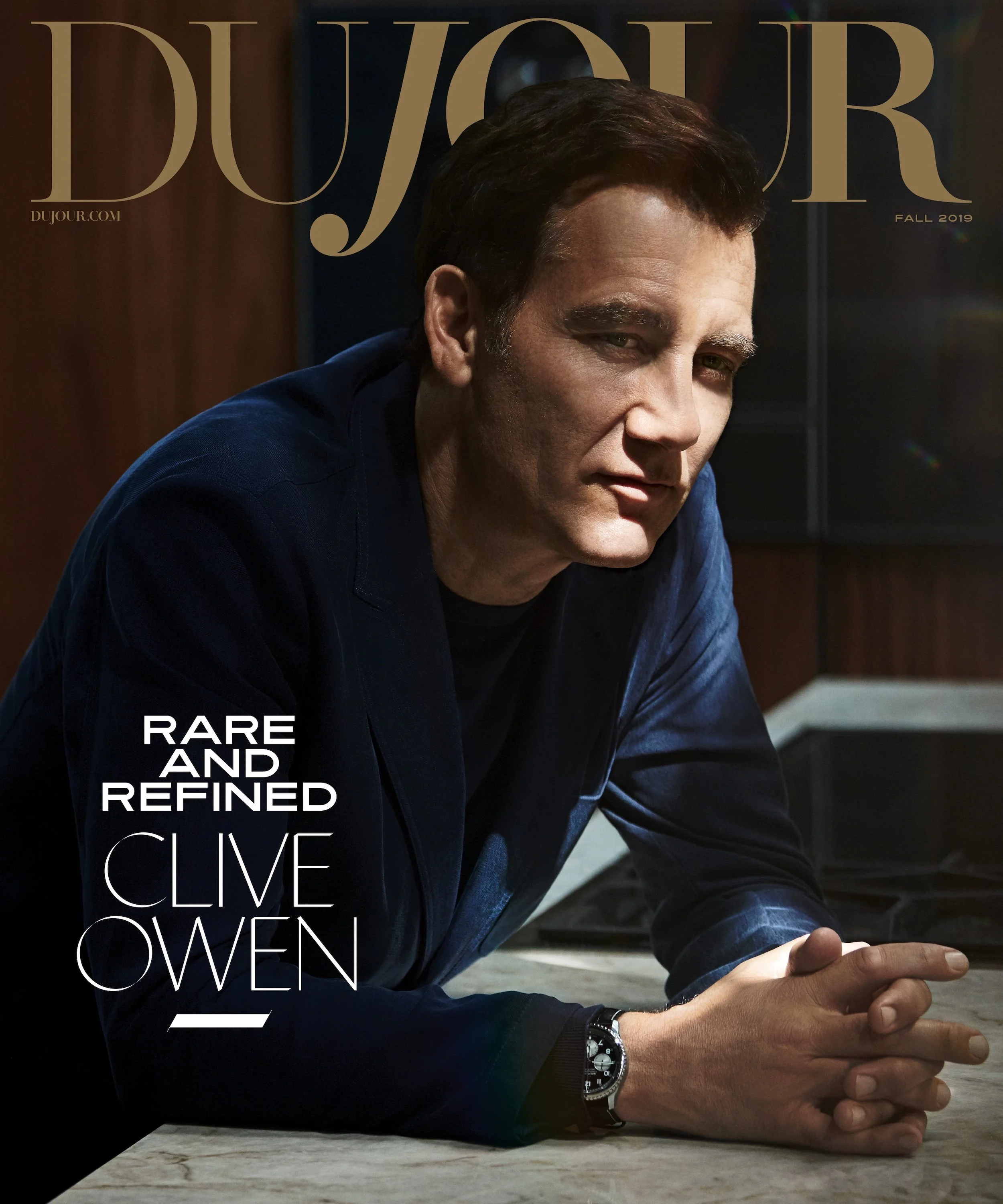 Cover of DuJour magazine featuring a close-up photo of actor Clive Owen wearing a dark blue jacket, resting his arms on a table, with text indicating the issue is Fall 2019 and describing him as "rare and refined."