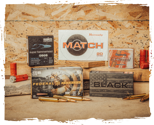 Various boxes and cartridges of ammunition, including handloaded and branded types, displayed on a wooden surface.