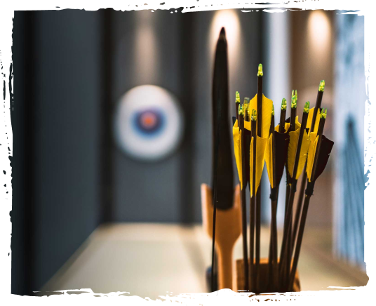 A collection of archery arrows in a yellow holder on a table, with a blurred archery target in the background.