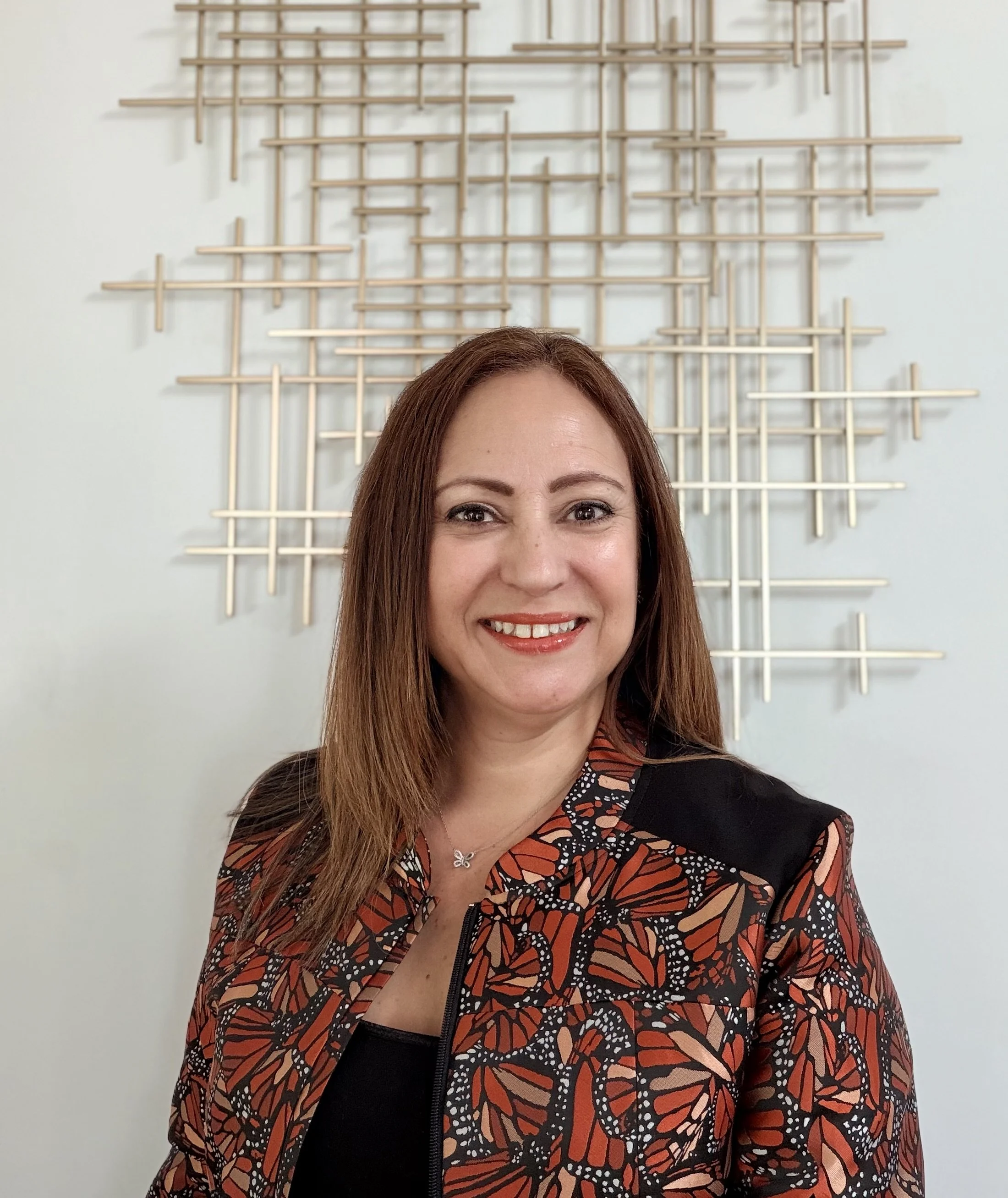 Maria D. Garate, Principal of Monarca People Transformation LLC, wearing a monarch butterfly-print blazer and smiling warmly