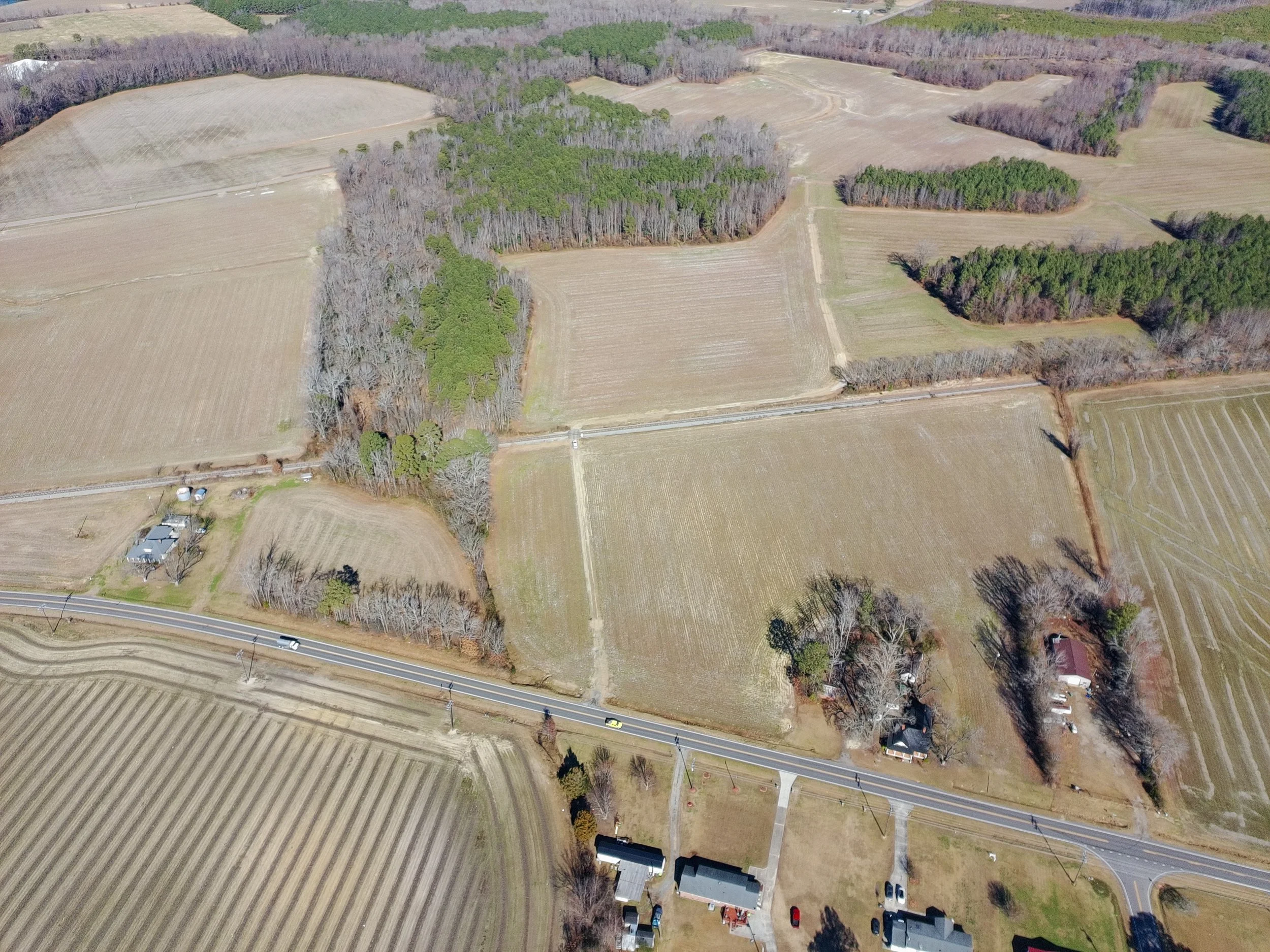 Aerial view of a rural area with farmland, trees, roads, and a few houses.