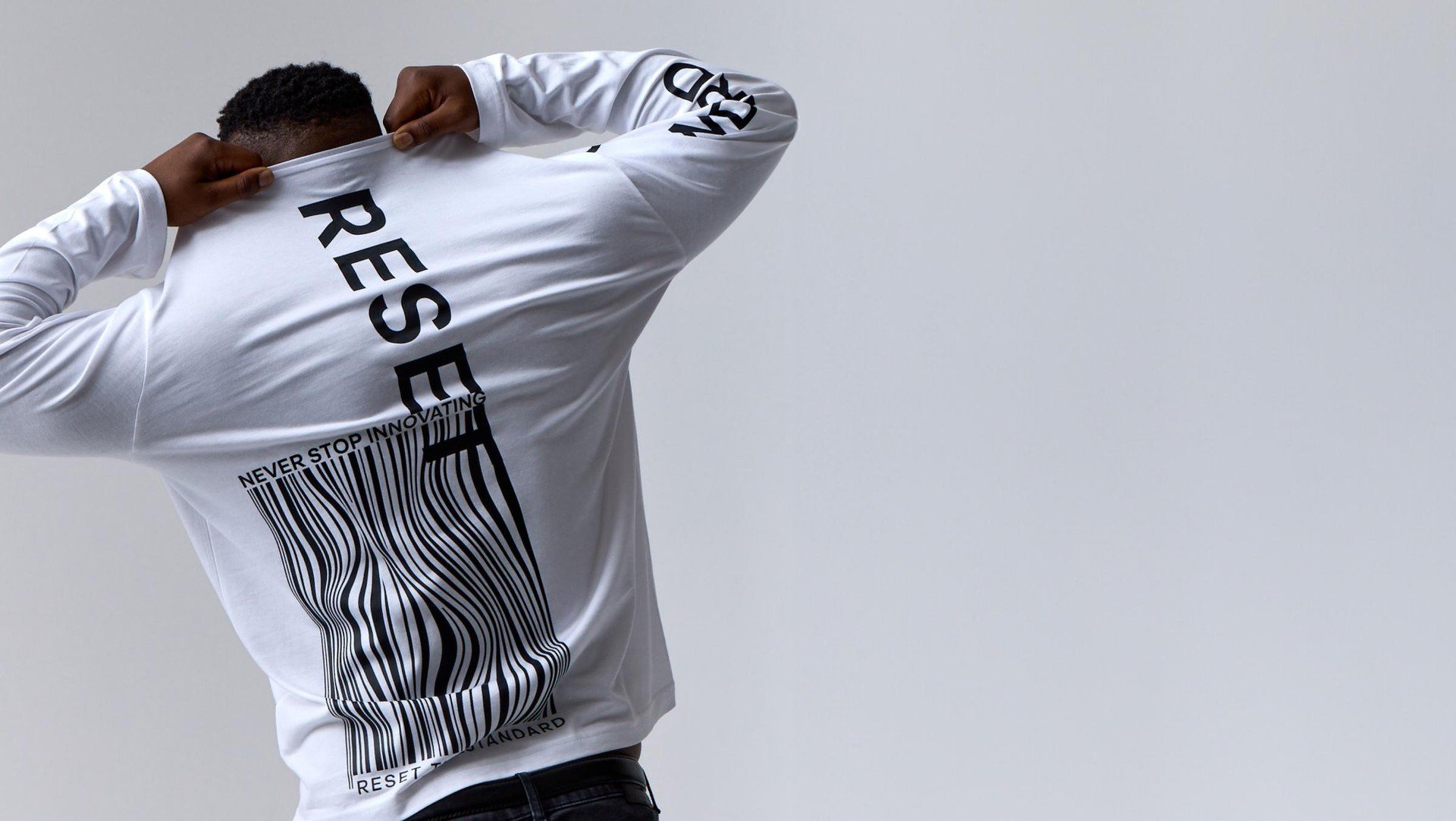 Person wearing a white long-sleeve shirt with black text and a barcode graphic, pulling the collar over their face against a plain gray background.