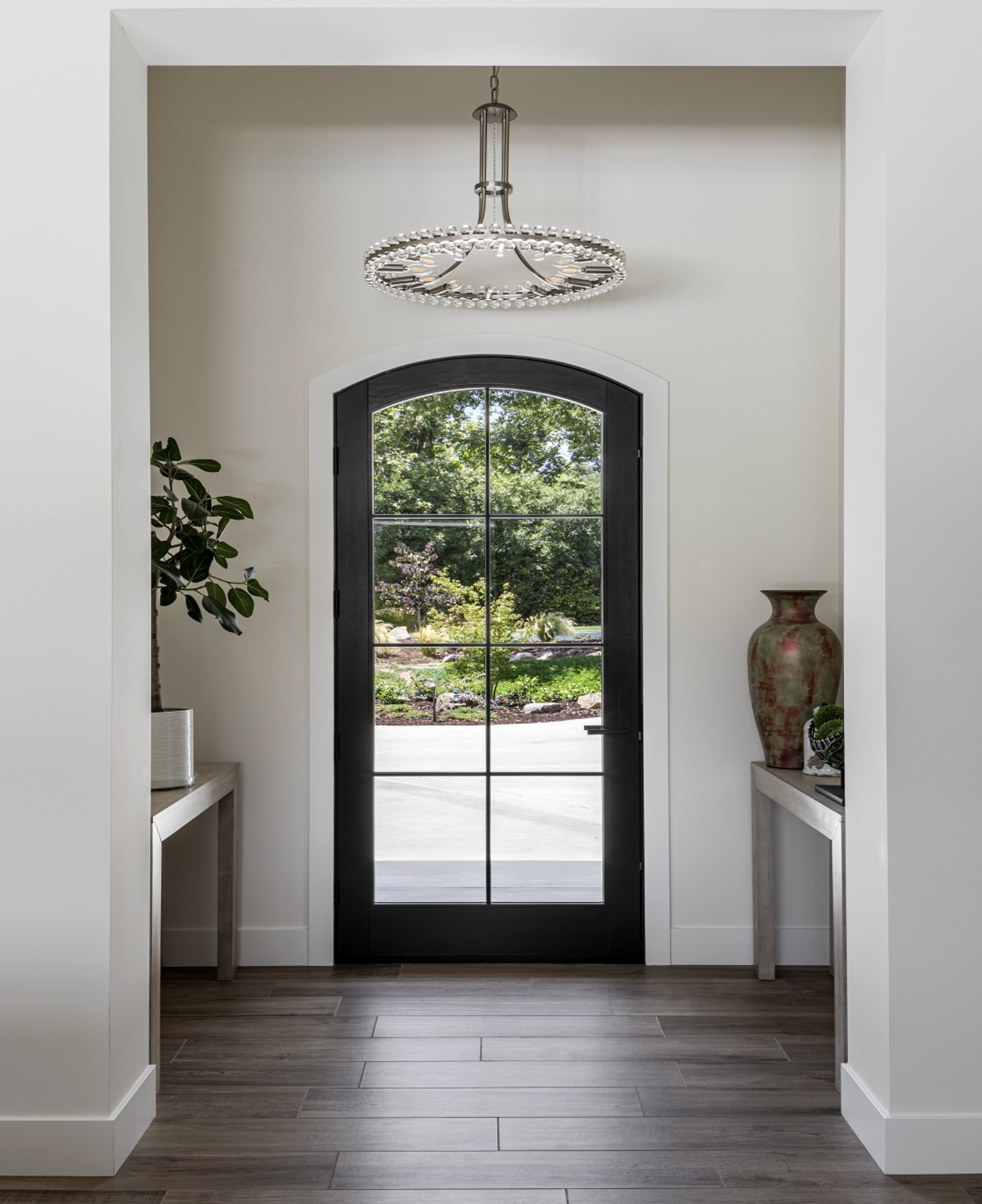 Interior entryway with black Andersen E-Series entry door, wooden floor, potted plant, decorative vases, and modern chandelier.
