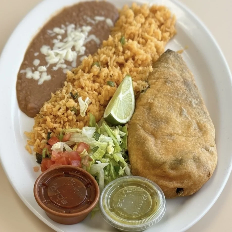 Plate of Mexican food with rice, refried beans topped with cheese, a fried chimichanga, shredded lettuce and tomato, lime wedge, and two small containers of green sauce and salsa.