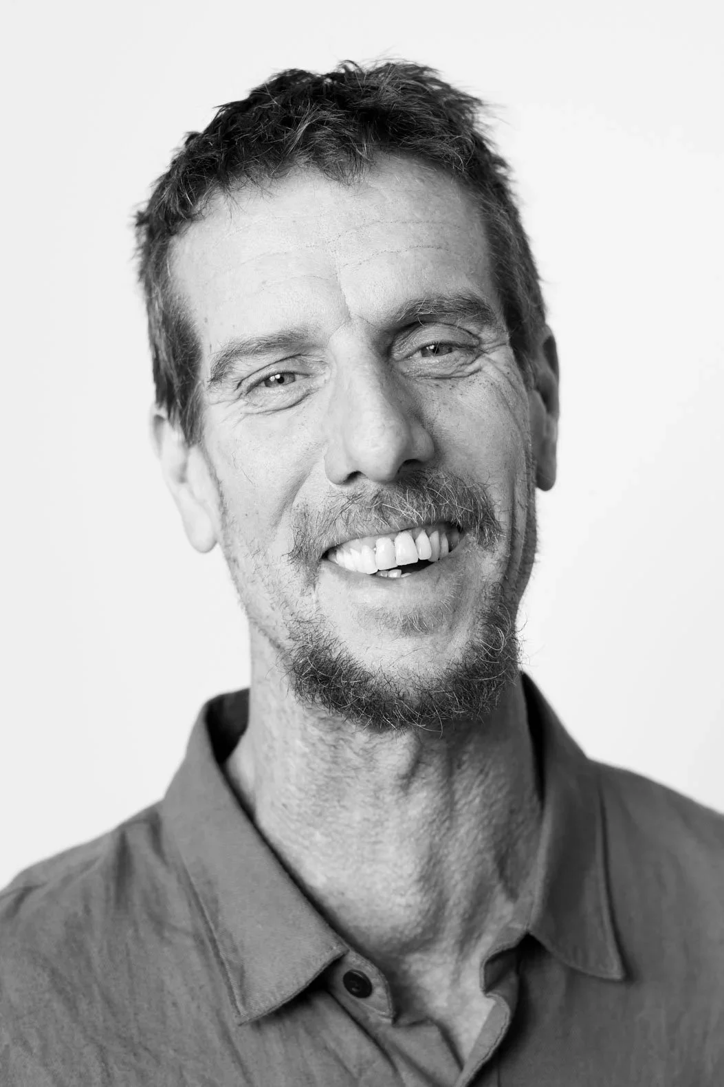 Black and white portrait of a smiling man with a beard, short hair, and wearing a collared shirt.