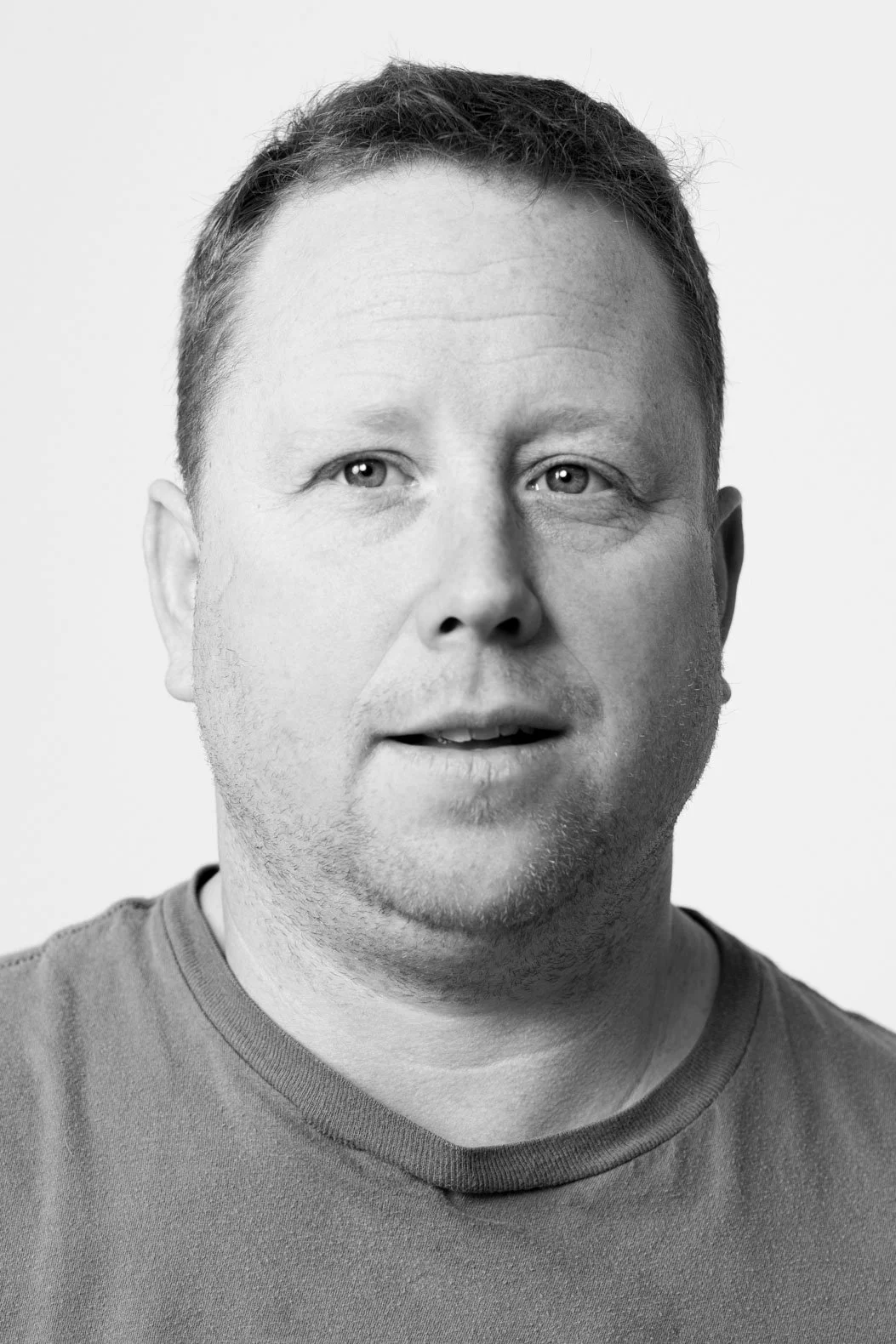 Close-up black and white portrait of a man with short hair, wearing a casual t-shirt, looking slightly to the right.