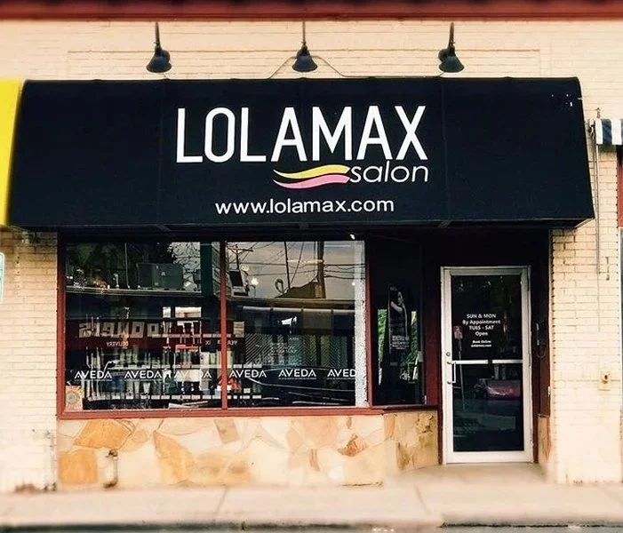 Exterior of a salon called LOLAMAX SALON with a black sign and white text, large windows, and a glass door.
