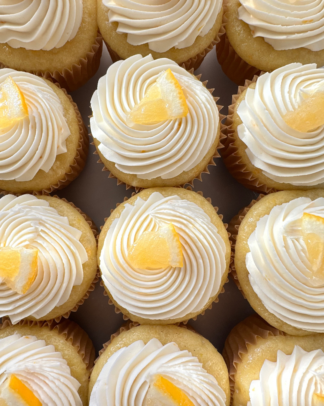Three vanilla cupcakes topped with swirl of pink and white frosting, each decorated with a fresh raspberry and a splash of berry sauce, on a white serving platter.