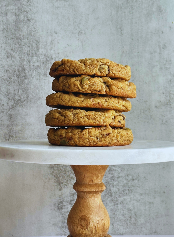 Stack of five oatmeal cookies on a white marble cake stand with a wooden base, against a textured background.