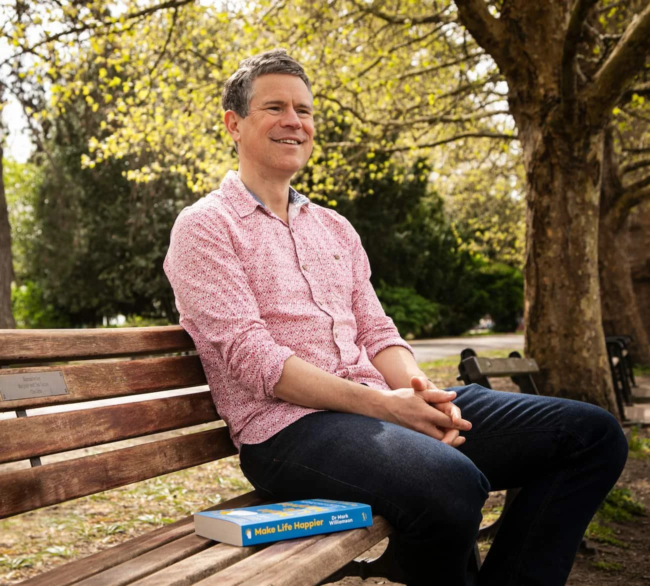 Dr Mark Williamson sat outside with Make Life Happier book