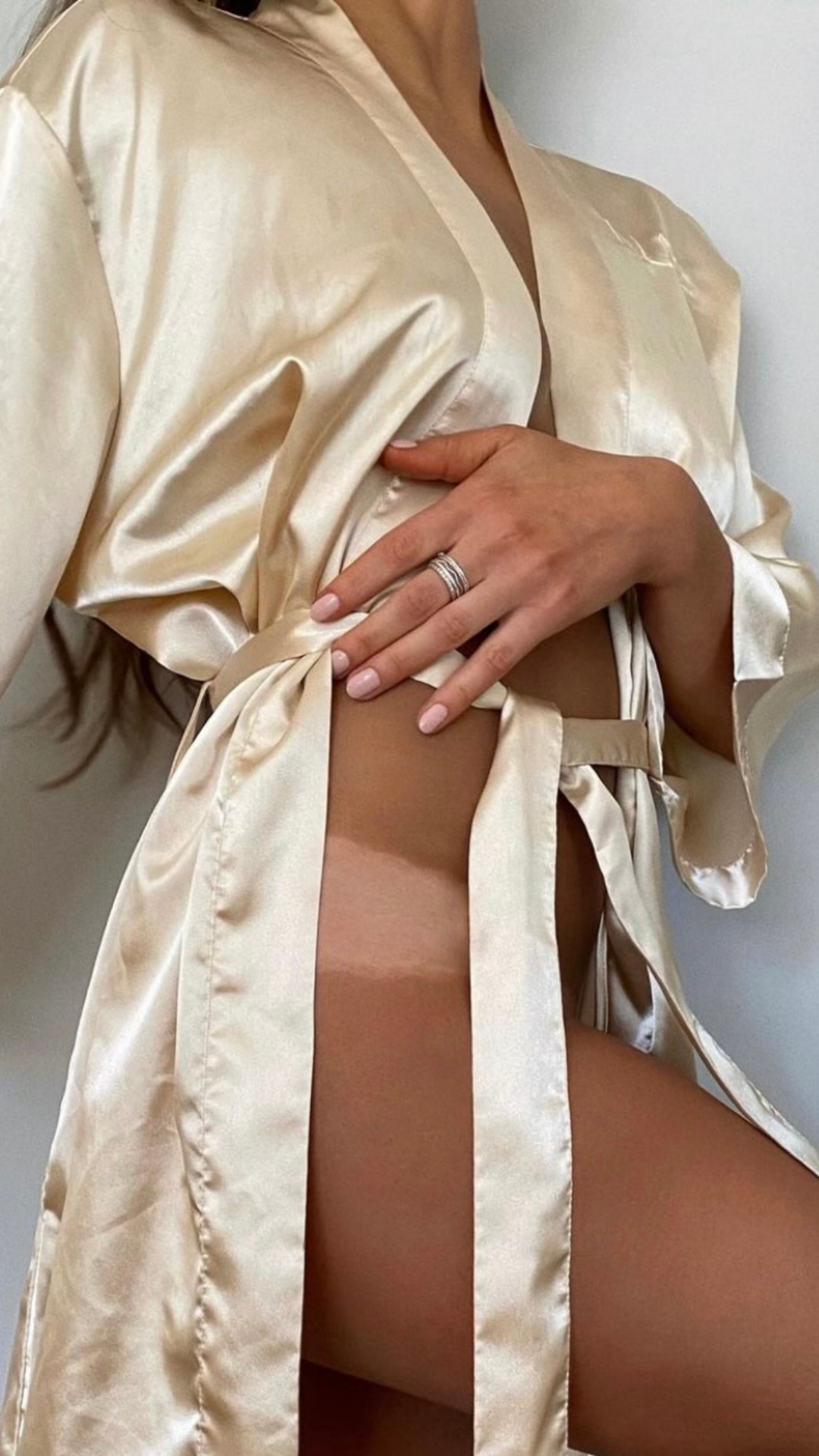 A person wearing a satin robe, revealing a part of their thigh and hand with a ring. The person's face is not visible.