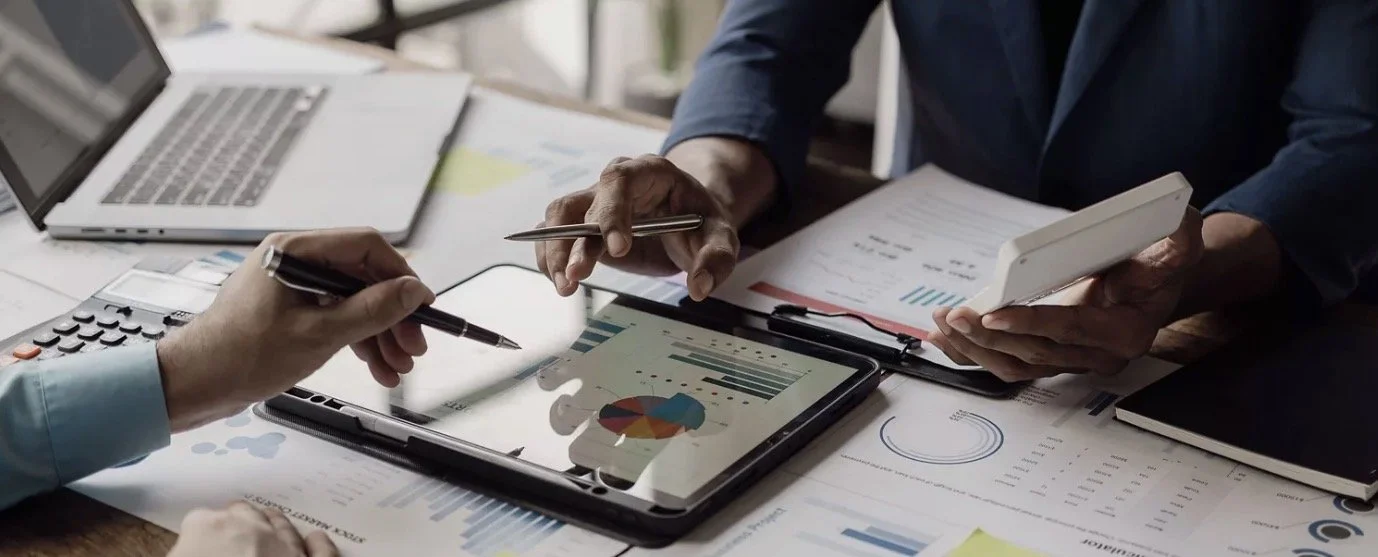 Two people working on a tablet with financial charts and documents on the table.