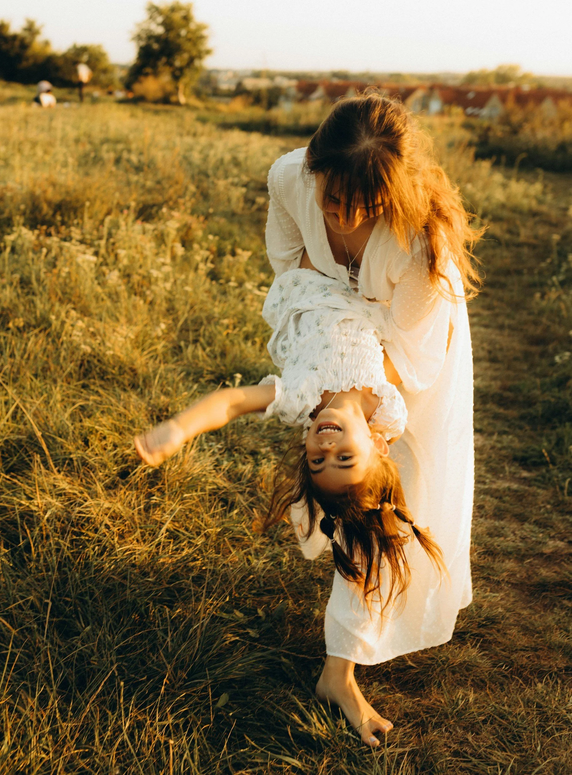 mother playfully carrying child upside-down in a sunlit meadow