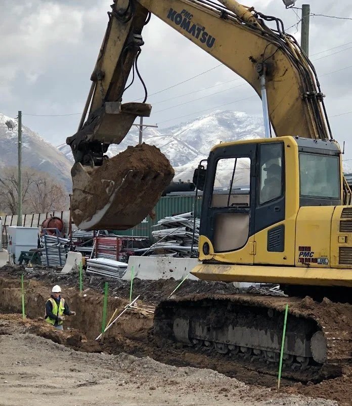 Construction excavator digging a trench at a construction site with mountains in the background.