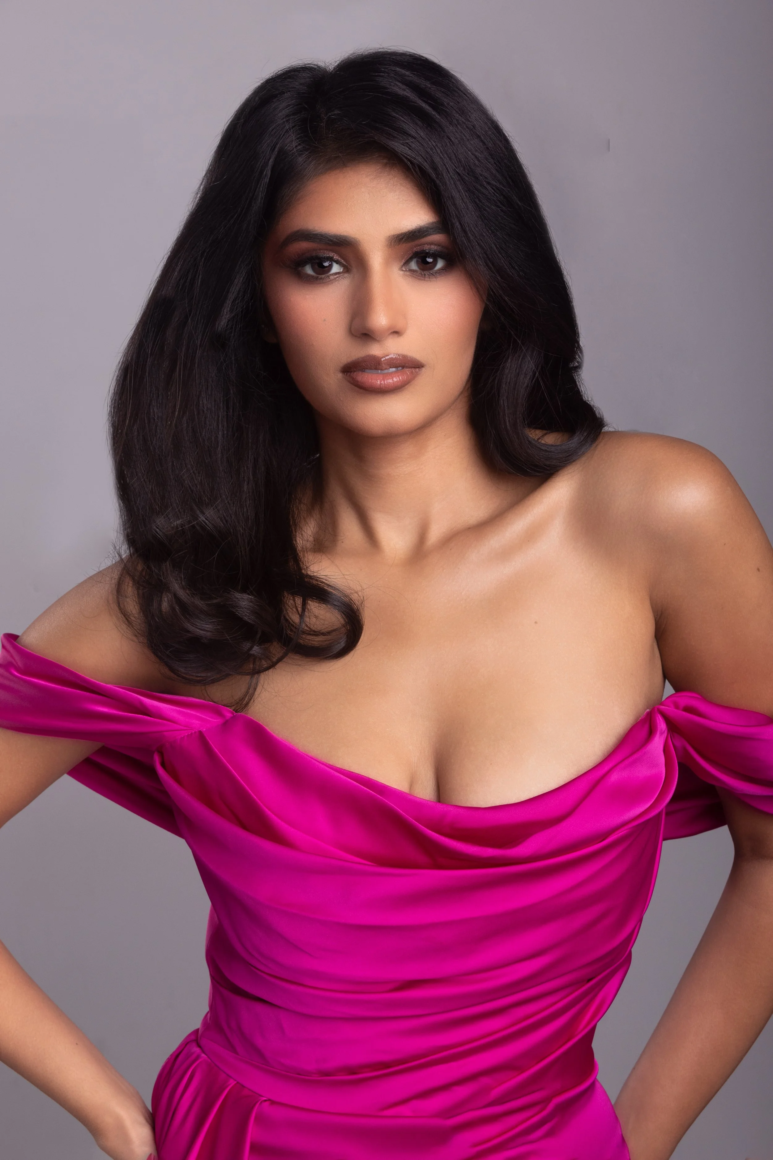 A woman with long black hair wearing a bright pink off-shoulder dress against a plain background.