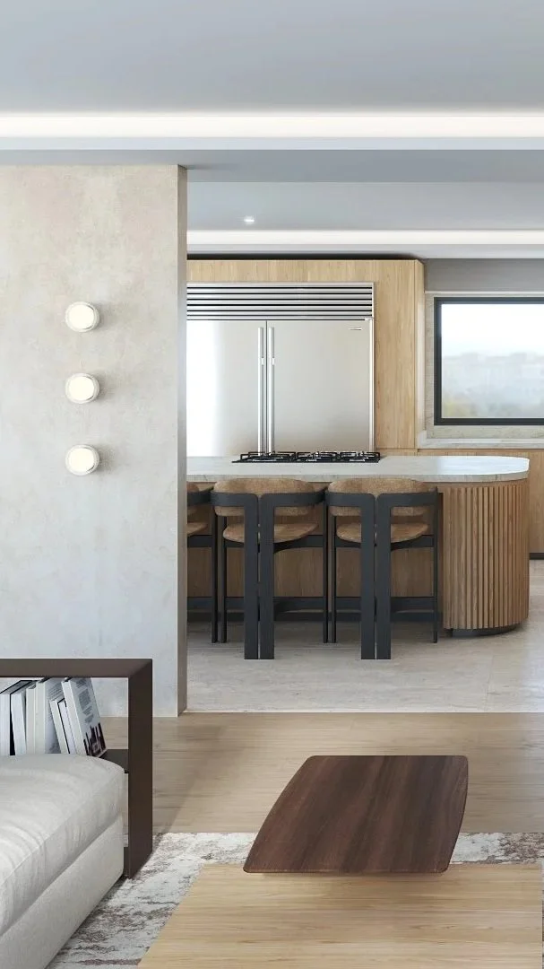 Vista de una cocina moderna con barra y sillas, nevera doble en el fondo, ventana grande y muebles de madera, con parte del salón visible.
