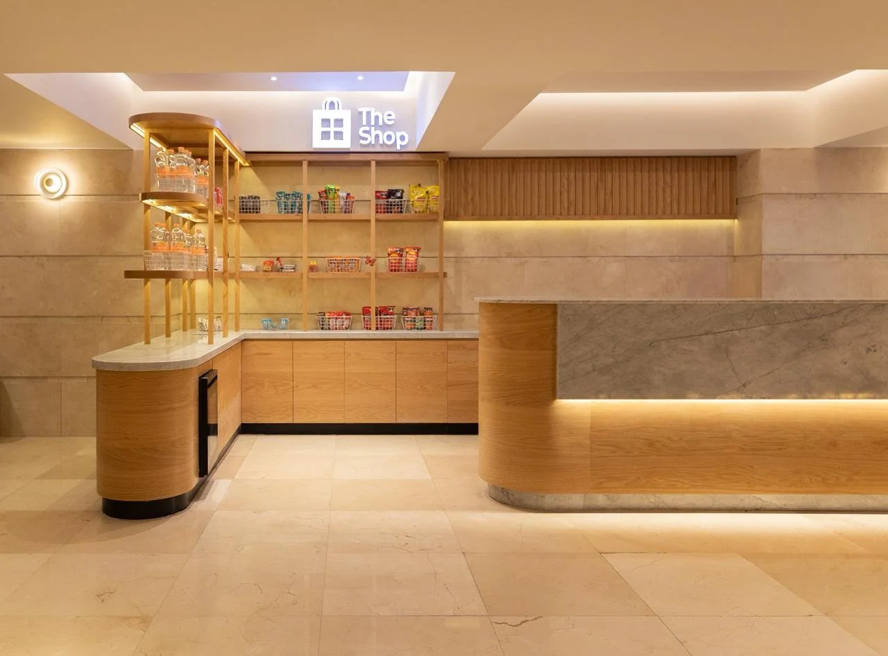 Mostrador de una tienda llamada 'The Shop' con estantes de madera y productos en bolsas de colores, en un ambiente moderno y bien iluminado.