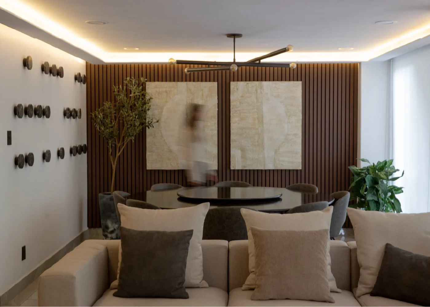 Sala de estar moderna con sillones blancos y almohadas, mesa redonda, paredes decoradas con cuadros grandes y discos de vinilo, plantas de interior, iluminación ambiental y un ventilador de techo