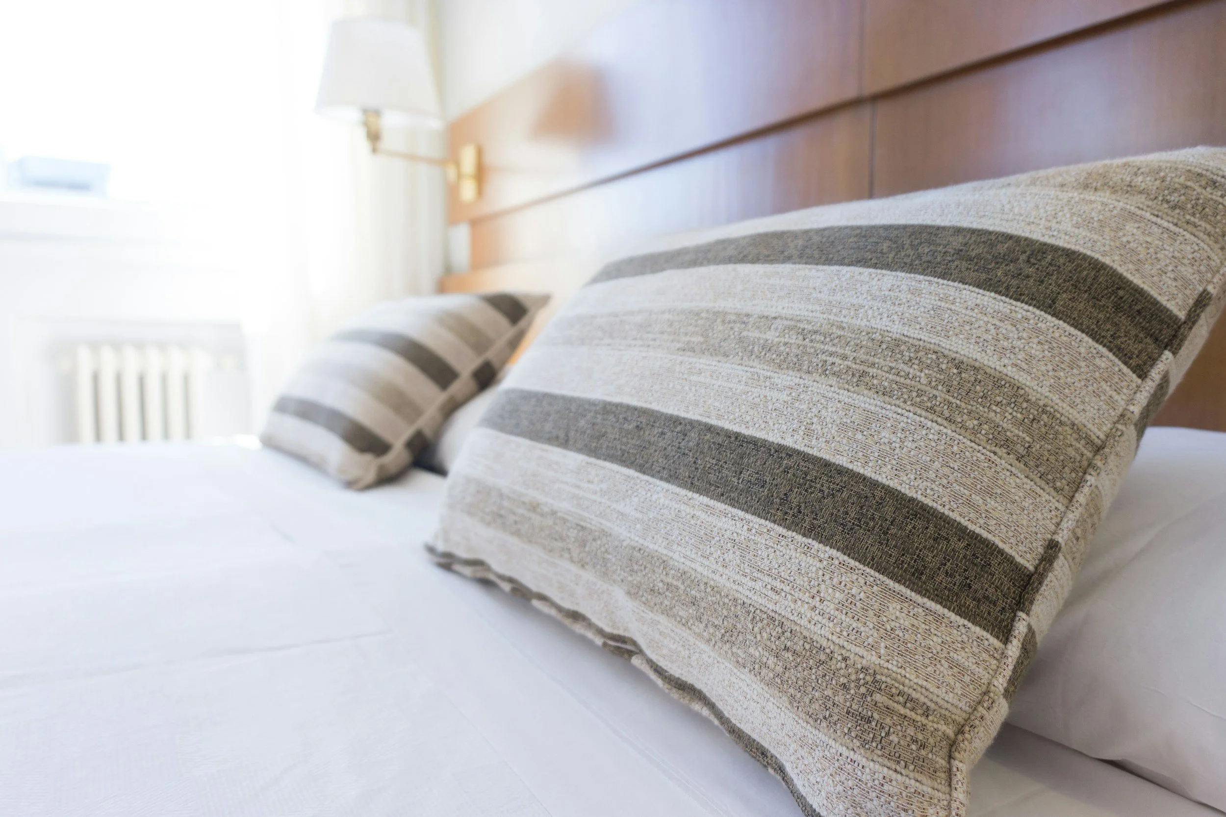 Close-up of a bed with striped beige and gray pillows in a bright, modern room.