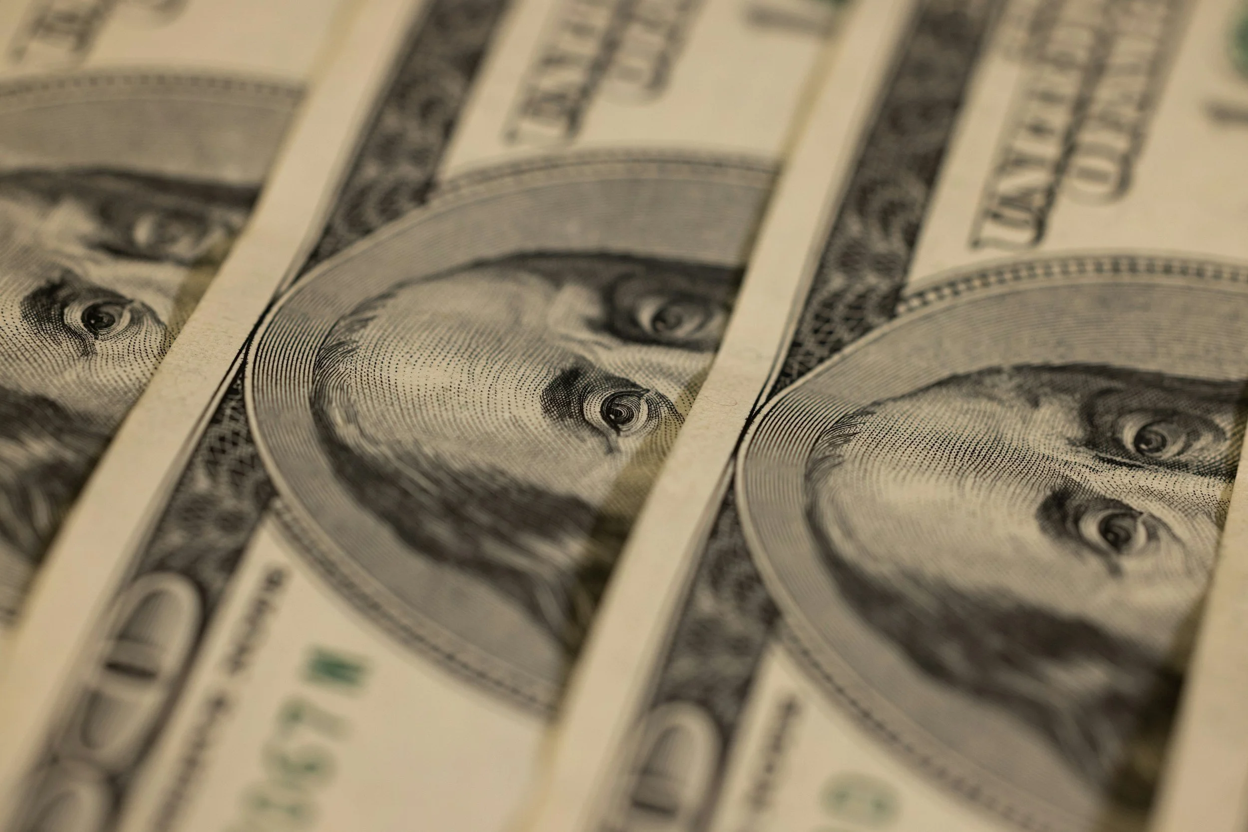 Close-up of multiple overlapping US hundred-dollar bills with Benjamin Franklin's portrait.
