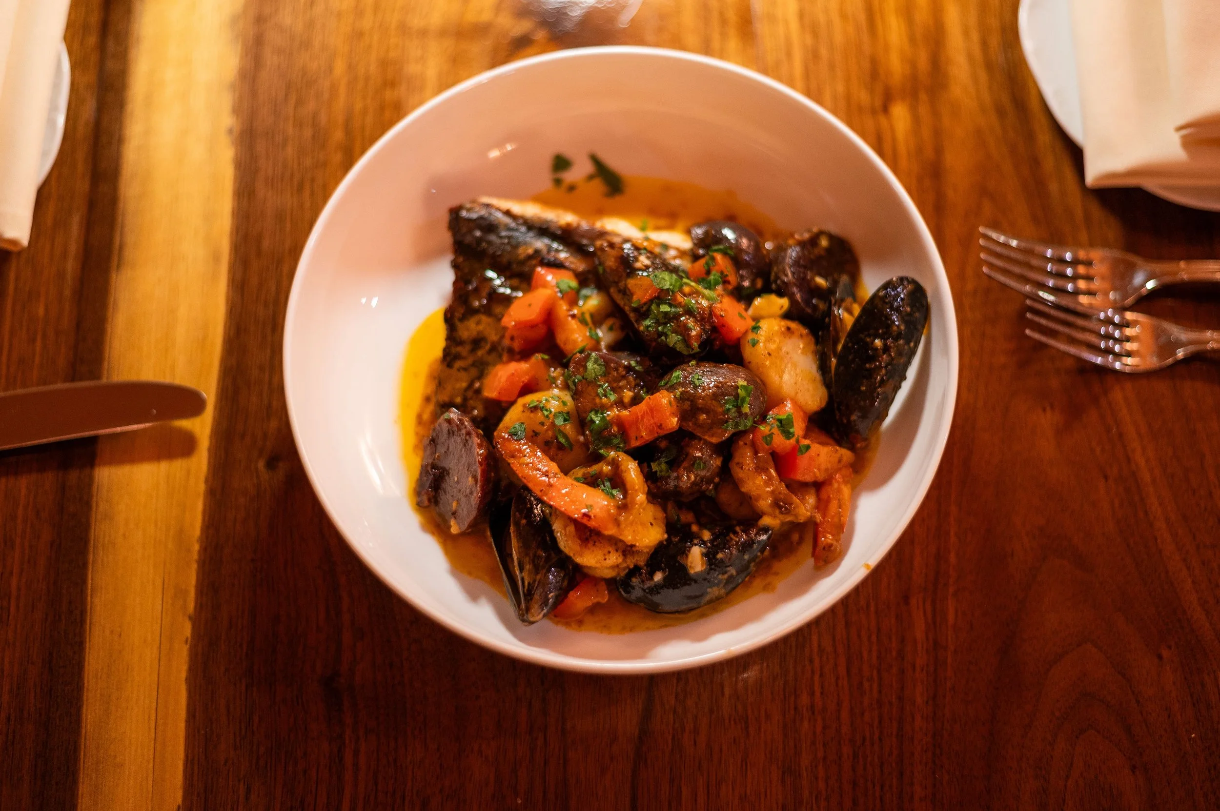 Plated appetizer of steamed mussels and shrimp in a savory tomato broth with fresh herbs, served at Bistro SOJO.