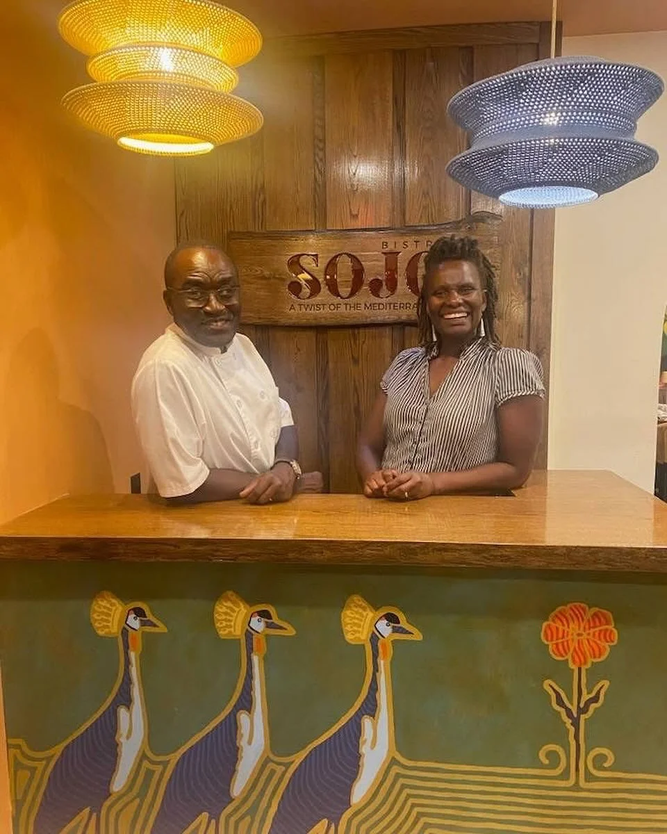 Felix and Martha Addison stand at the front of SOJO Bistro in front of a sign that reads "SOJO - A Twist of the Mediterranean."