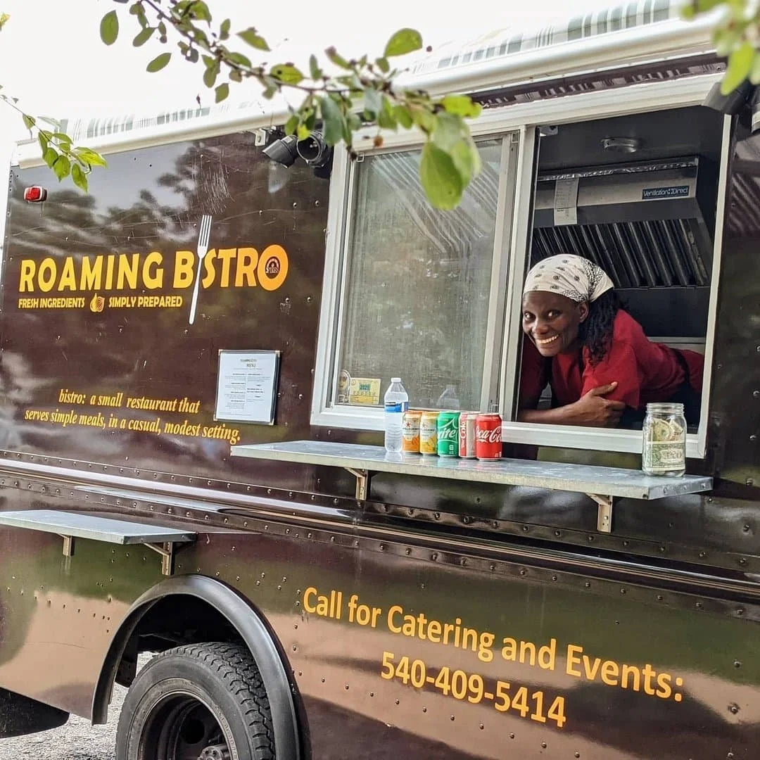Martha Addison, the co-owner, pokes her head out of the "Roaming Bistro" food truck window and smiles. The food truck is labeled 'Roaming Bistro' and offers catering and event services.