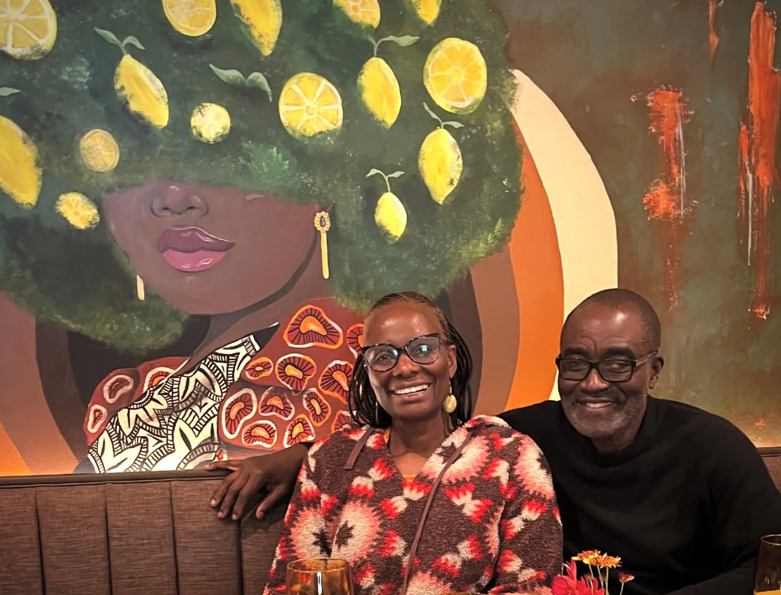 Owners of Bistro SOJO - Martha and Felix sit inside of the restaurant in front of the signature mural of a woman with lemons in hair.