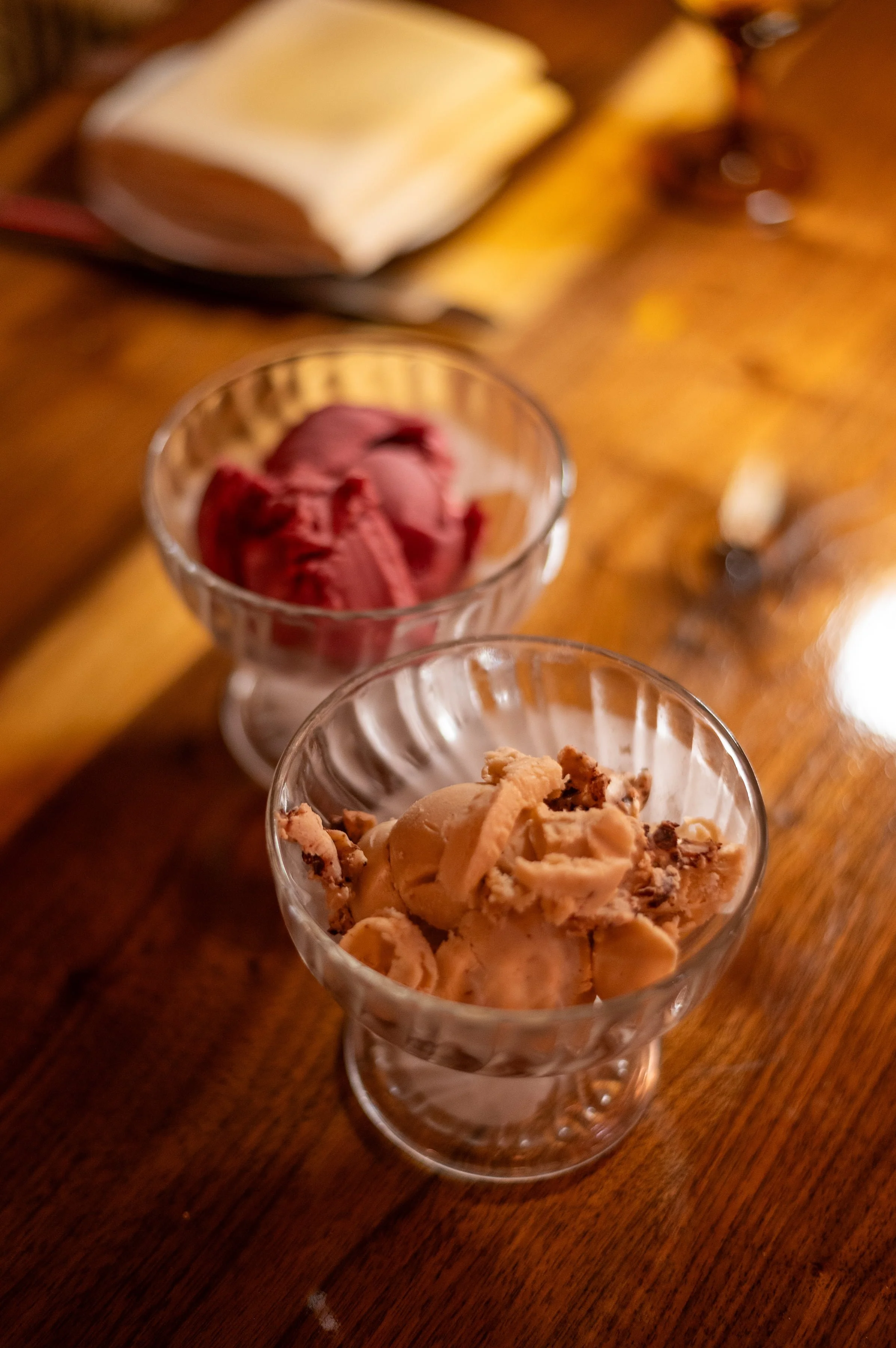 Two glass bowls of artisanal gelato—one berry sorbet and one salted caramel—on a wooden bistro table.