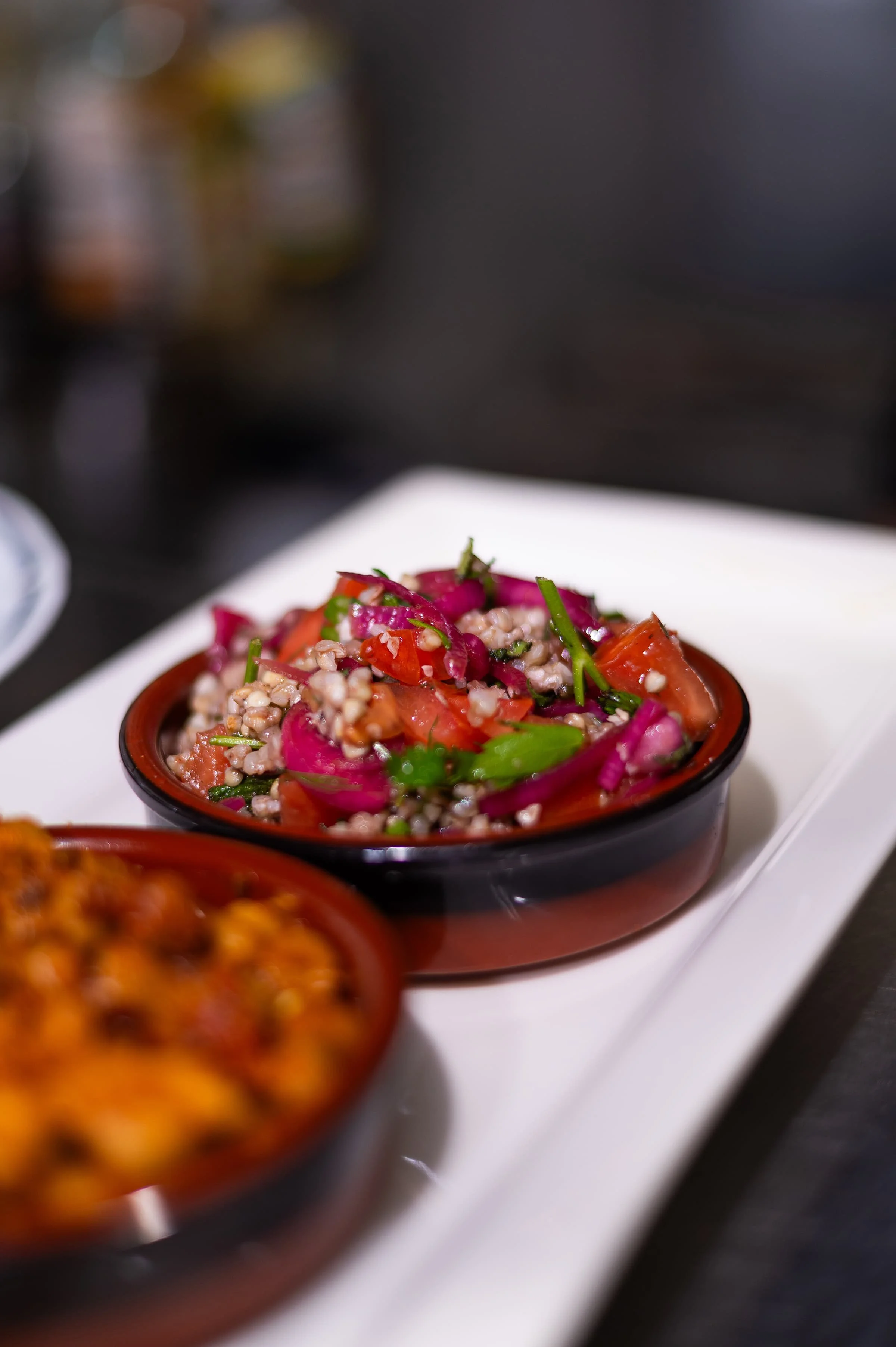 Close-up of a bowl containing a colorful salad with grains, chopped tomatoes, red onions, and herbs.