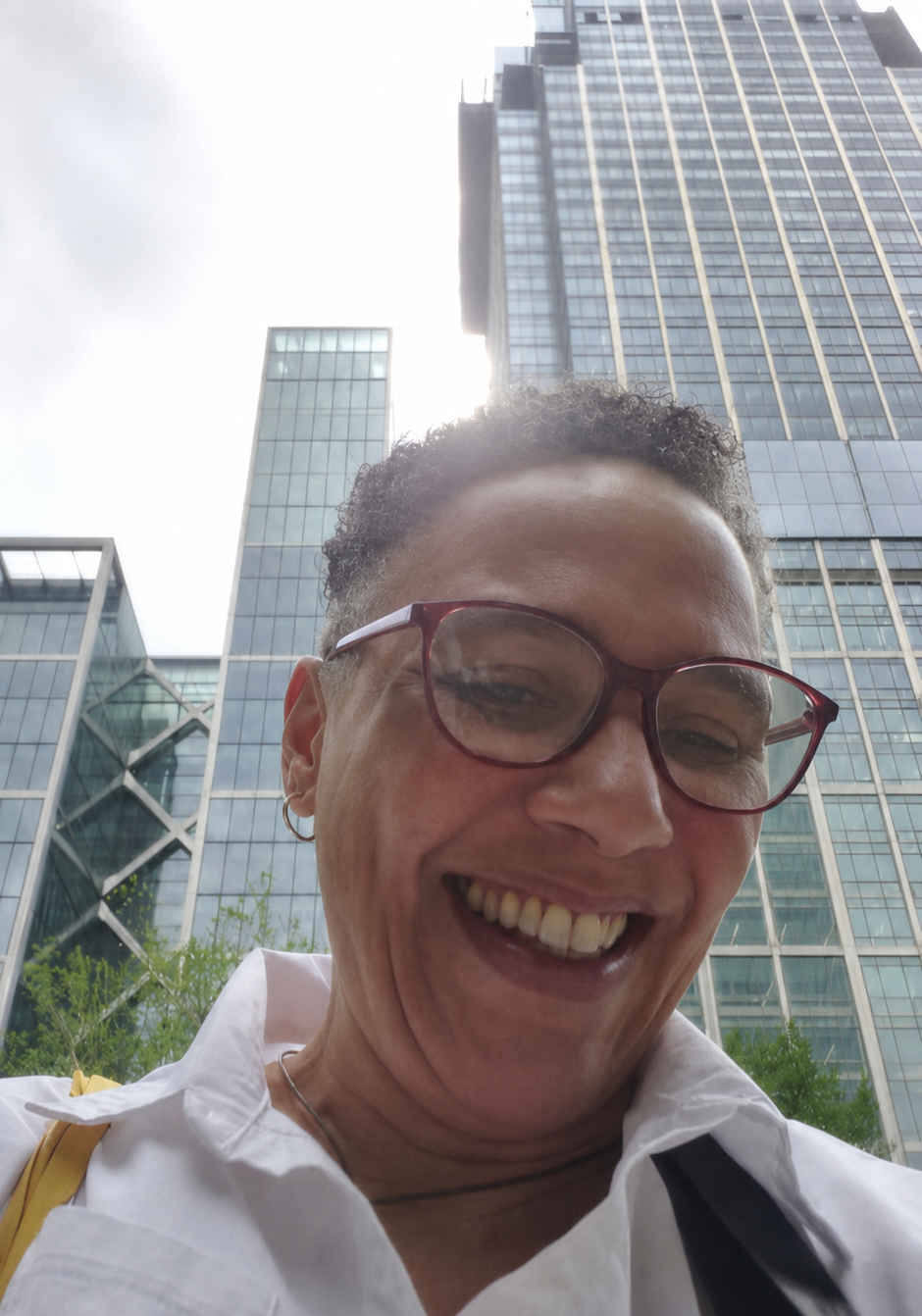 A woman smiling and looking down at the camera with tall glass skyscrapers behind her.