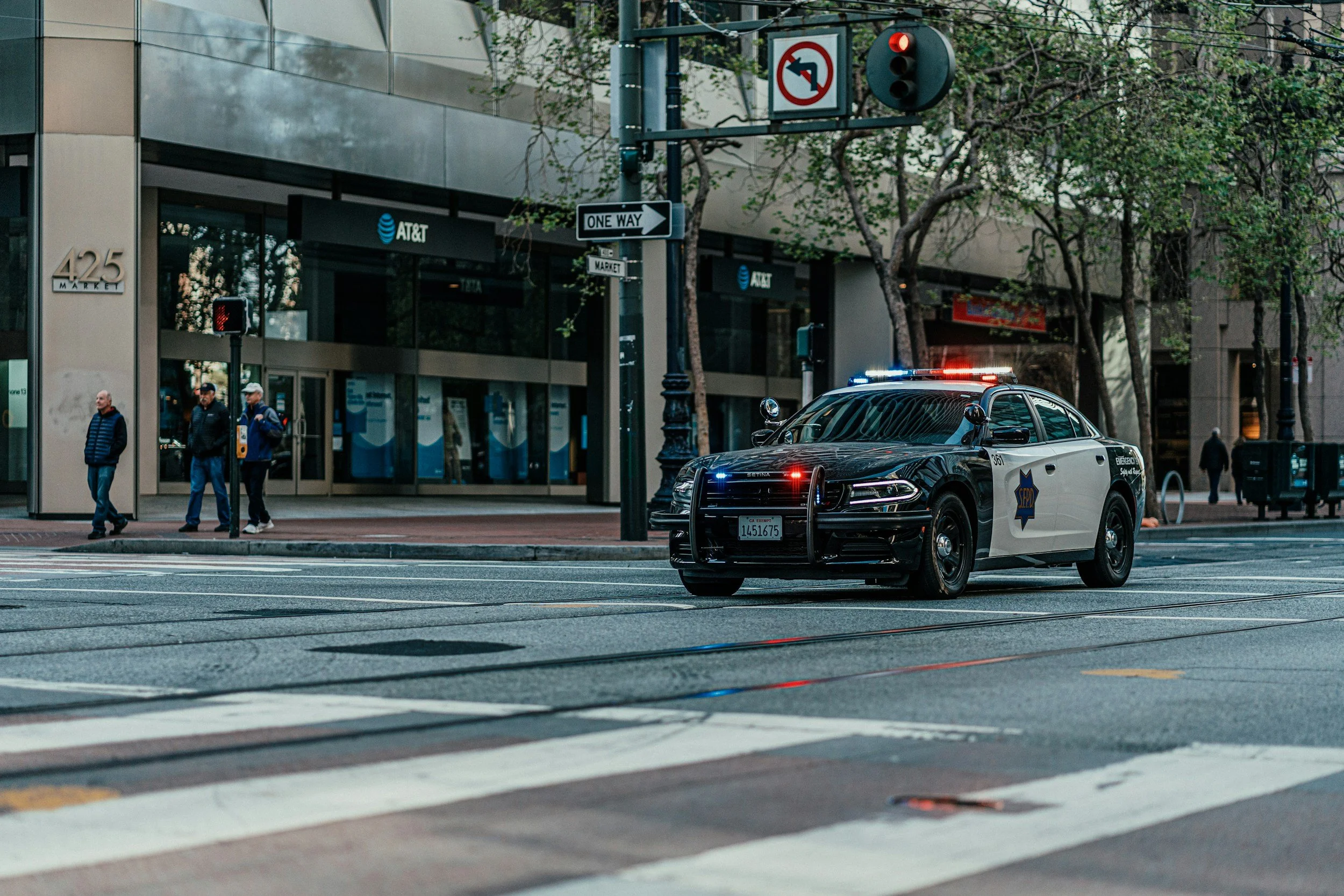 image of downtown san jose. there is a red light and a poliece car is the only visible car on the road with their lights on.