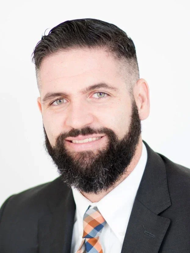 Portrait of a smiling man, Of Counsel Patrick M. Coughlin, with a beard, wearing a suit and a colorful striped tie, against a white background.