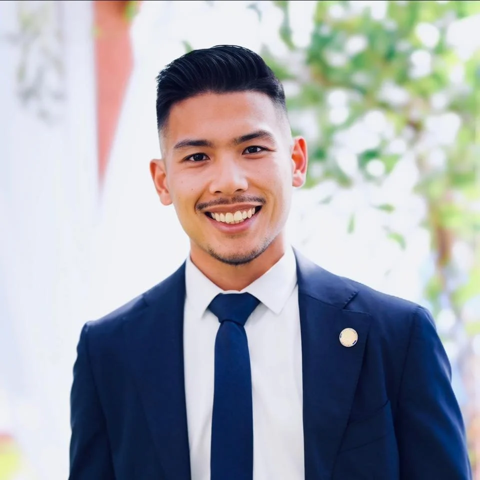 Professional headshot of Lou Anthony Limon attorney at law. He is wearing a navy suit with a white button up and navy tie. He has big bright welcoming smile on his face.