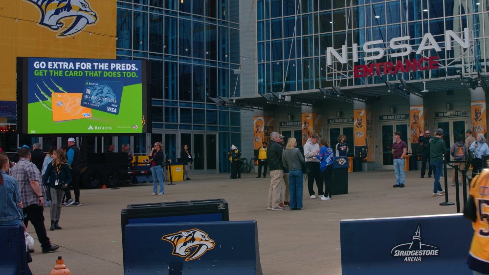 People lined up outside the Nissan Arena entrance, with a large digital billboard advertising credit cards and a sign for Bridgestone Arena.