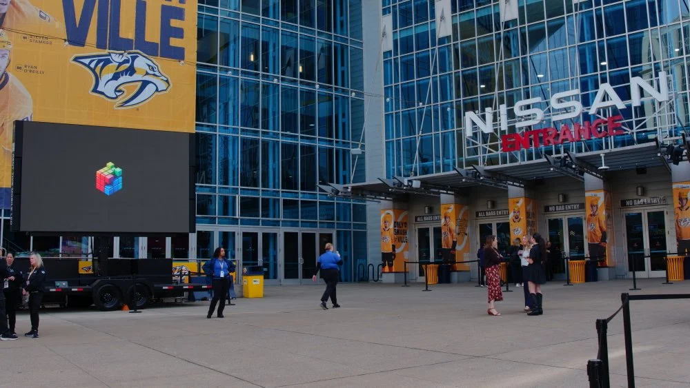 Exterior of a Nissan Arena with people standing outside, large digital billboard, and Nissan signage.