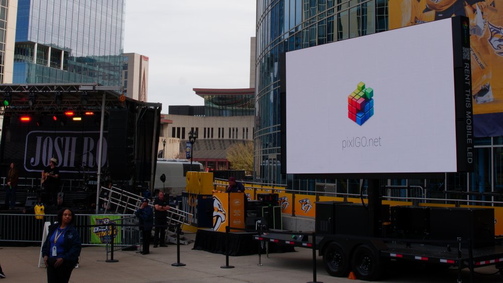 Outdoor event with a stage, a large LED screen displaying the pixelGO.net logo, and Nashville Predators banners in the background.