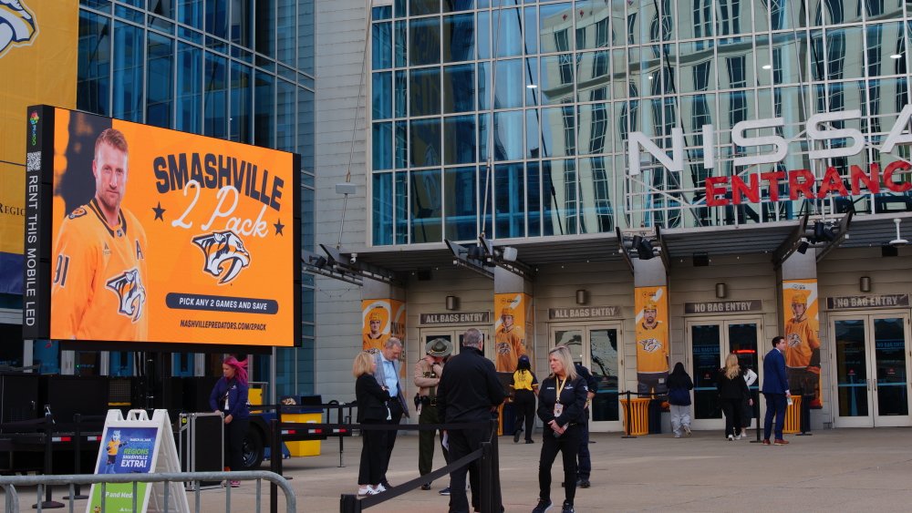 Exterior of Nissan Entrance with large digital billboard promoting Nashville Predators hockey tickets, people entering and outside the arena.
