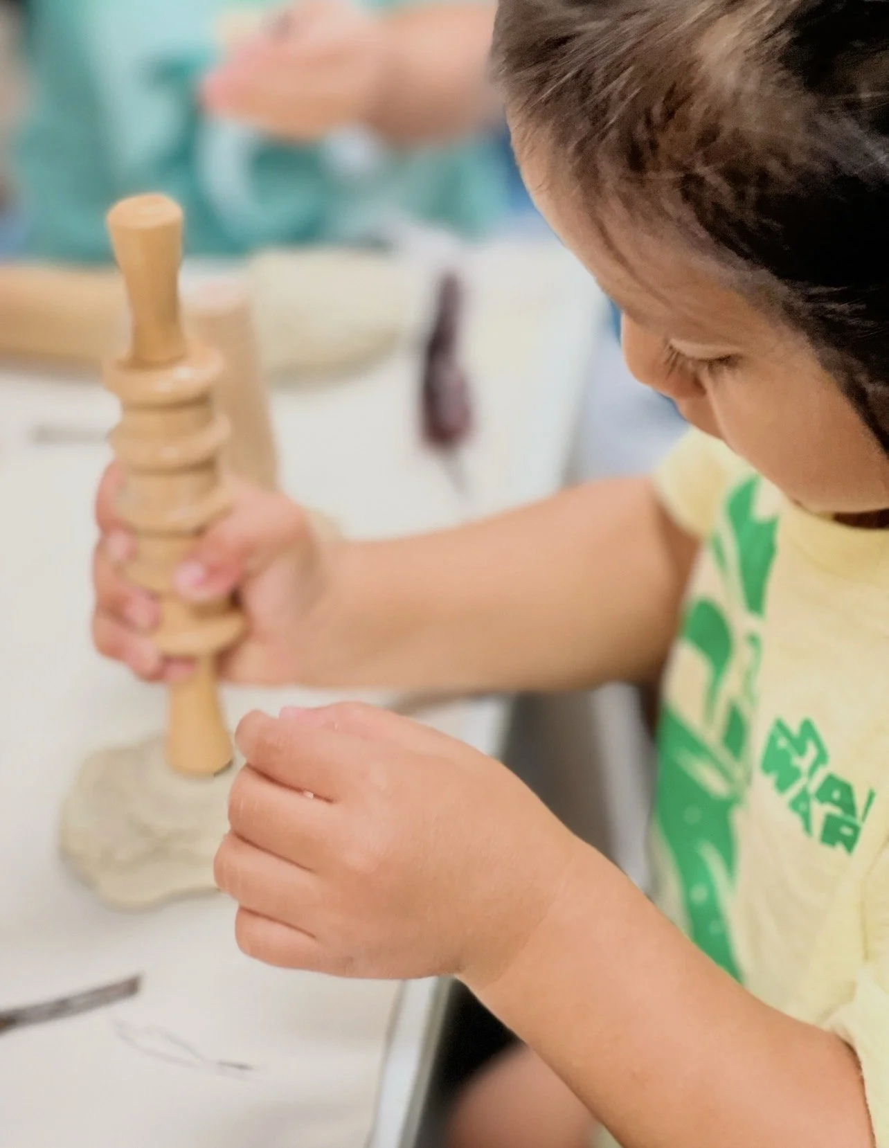 A child using a wooden mortar and pestle to grind or mash something, with focus on the child's hands and face.