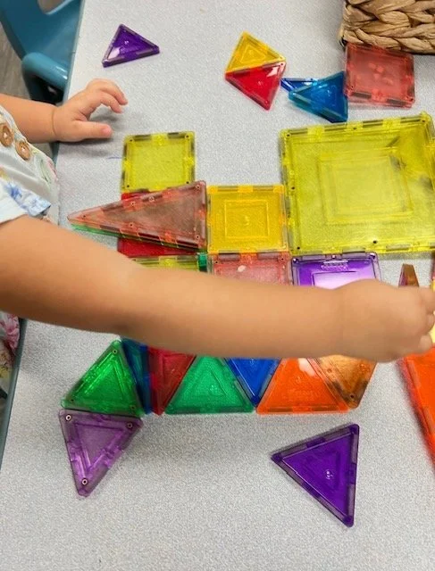 Child playing with colorful magnetic building tiles on a table, creating various geometric shapes.