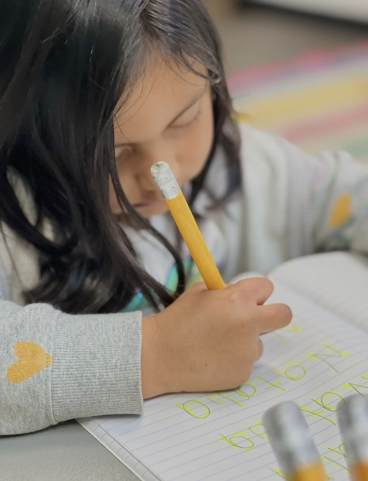 A young girl writing in a notebook with a yellow pencil, focusing on her work.