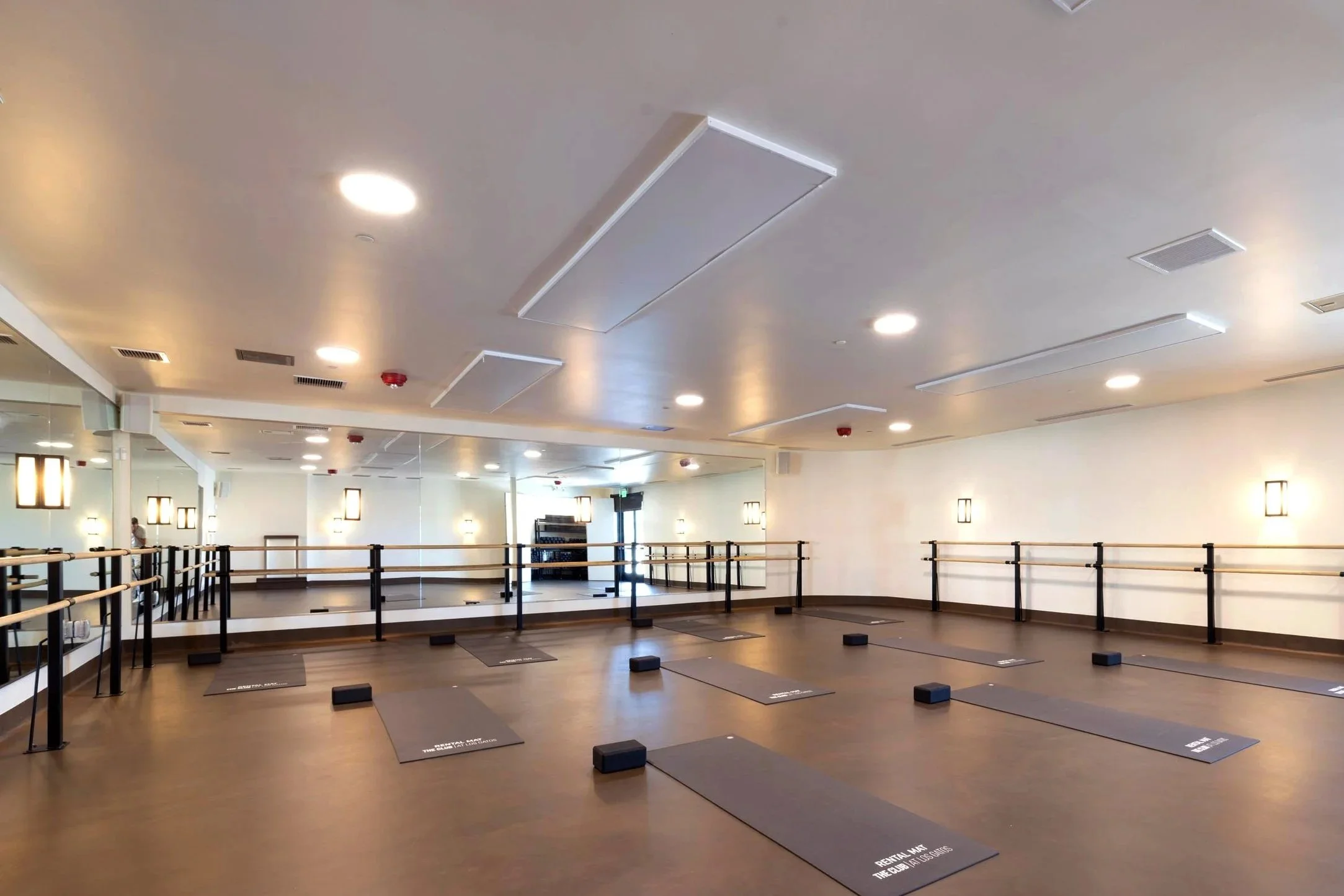 Dance studio with mirrors on the wall, ballet barres, ballet slippers, and black mats labeled 'Reception Mat' arranged on a wooden floor.
