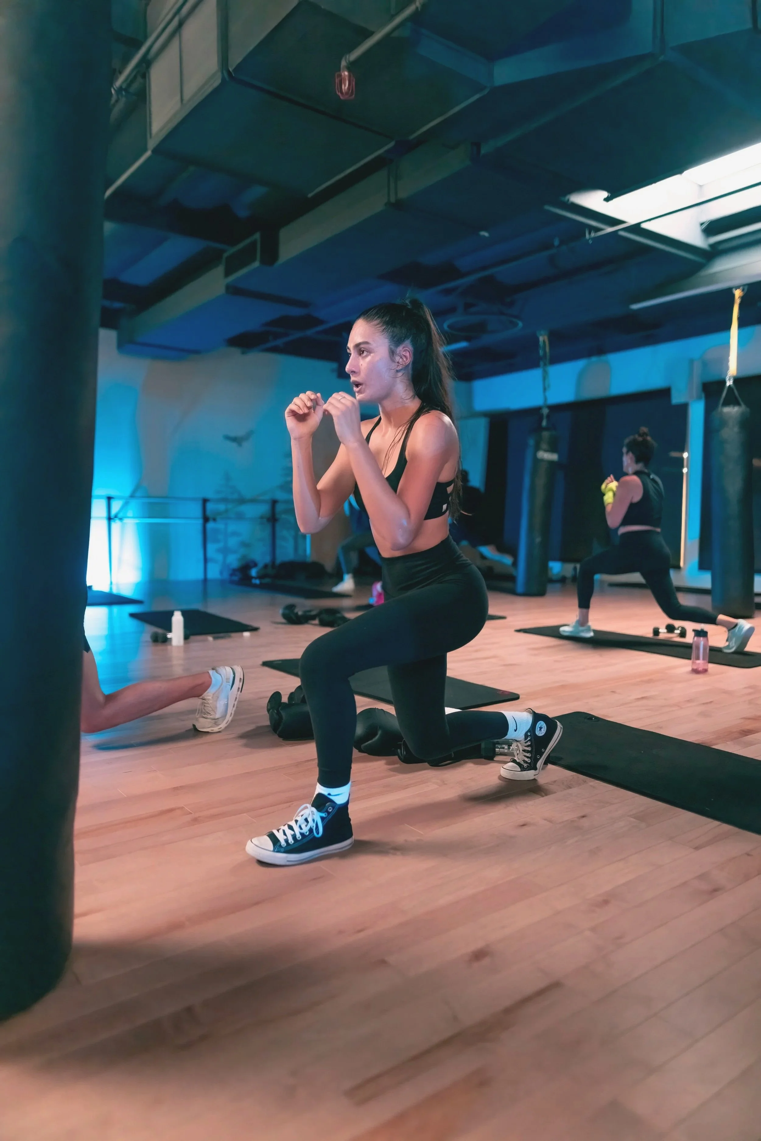 Woman in athletic wear doing lunges during a workout class in a gym.
