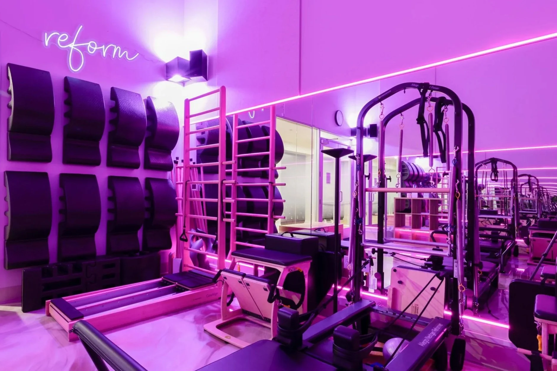 Gym equipment in a fitness studio illuminated with pink and purple neon lights.